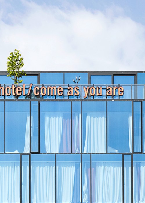 The exterior of the top of a hotel with floor to ceiling glass windows and a balcony terrace on the top floor